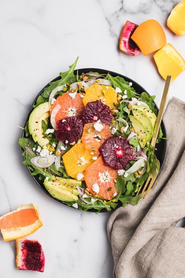 A fully plated avocado citrus salad bursting with color and garnished with seeds.