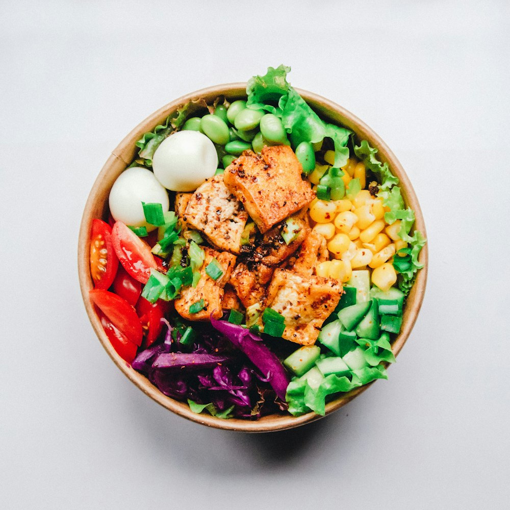 A wooden bowl of green edamame beans next to blocks of fresh white tofu.