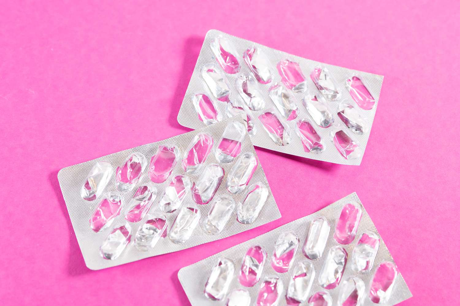 Multiple empty pill blister packs scattered on a pink background.