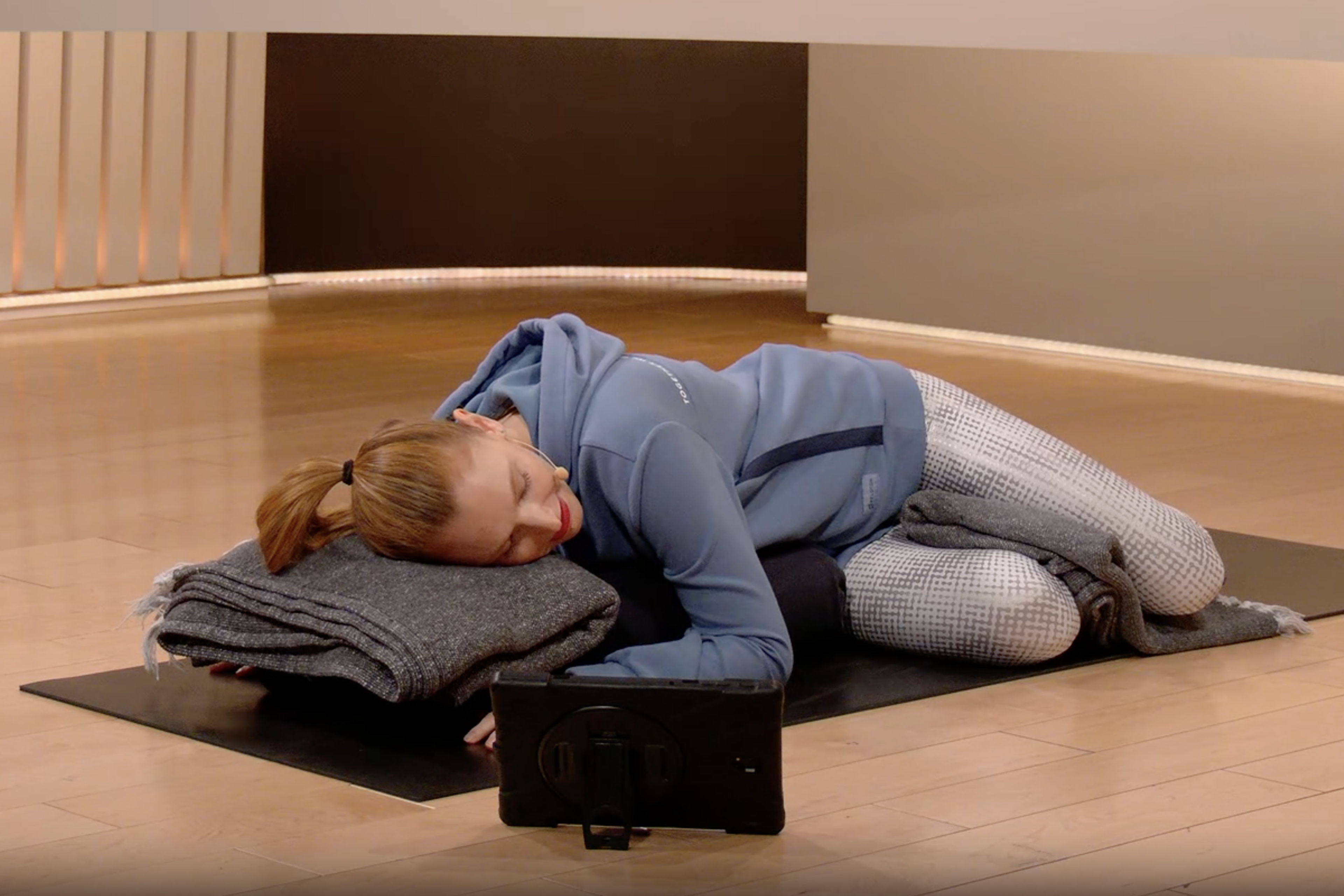 A woman performing a gentle spinal twist while resting her torso on a long yoga bolster.