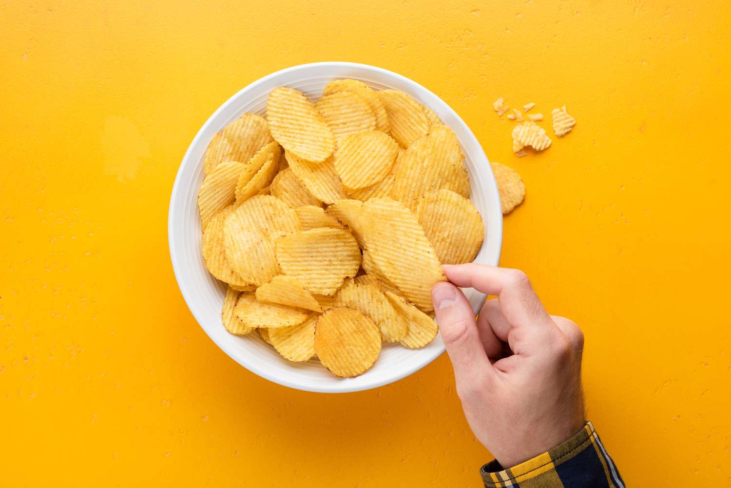 A close-up view of a person reaching for a potato chip in a bowl.