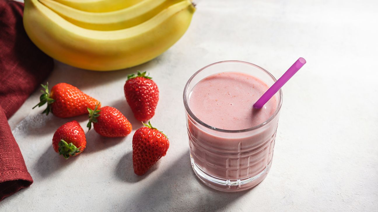 A glass of pink strawberry banana protein smoothie topped with a fresh strawberry.