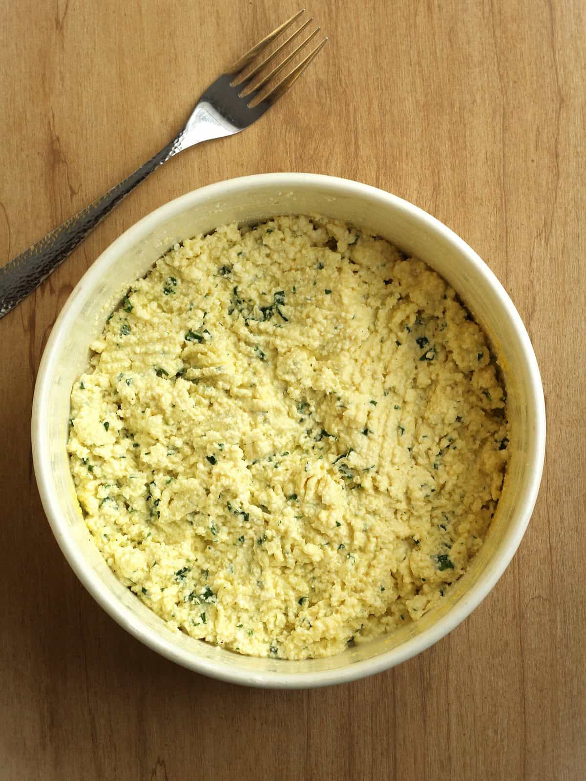 A close-up of ricotta fritter batter mixed in a bowl, showing a thick and textured consistency.