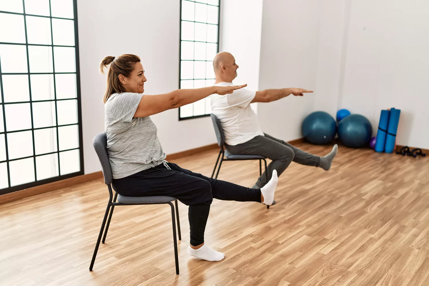 A woman performing a tree pose while holding onto the back of a chair for stability.