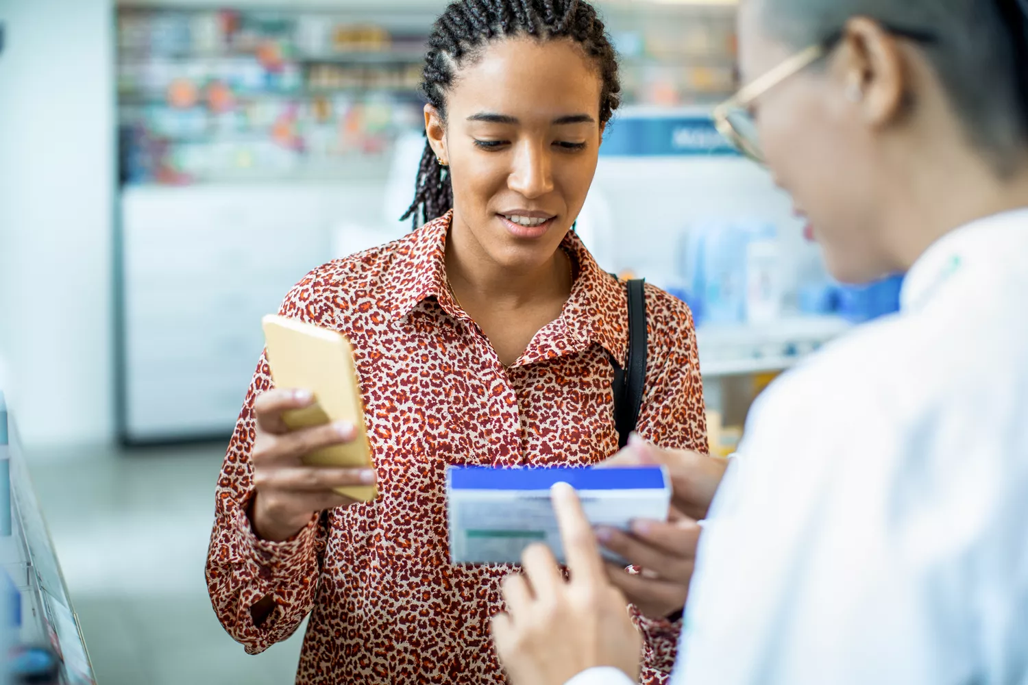 A customer in a pharmacy setting discussing a medical device box with a pharmacist wearing a white coat.