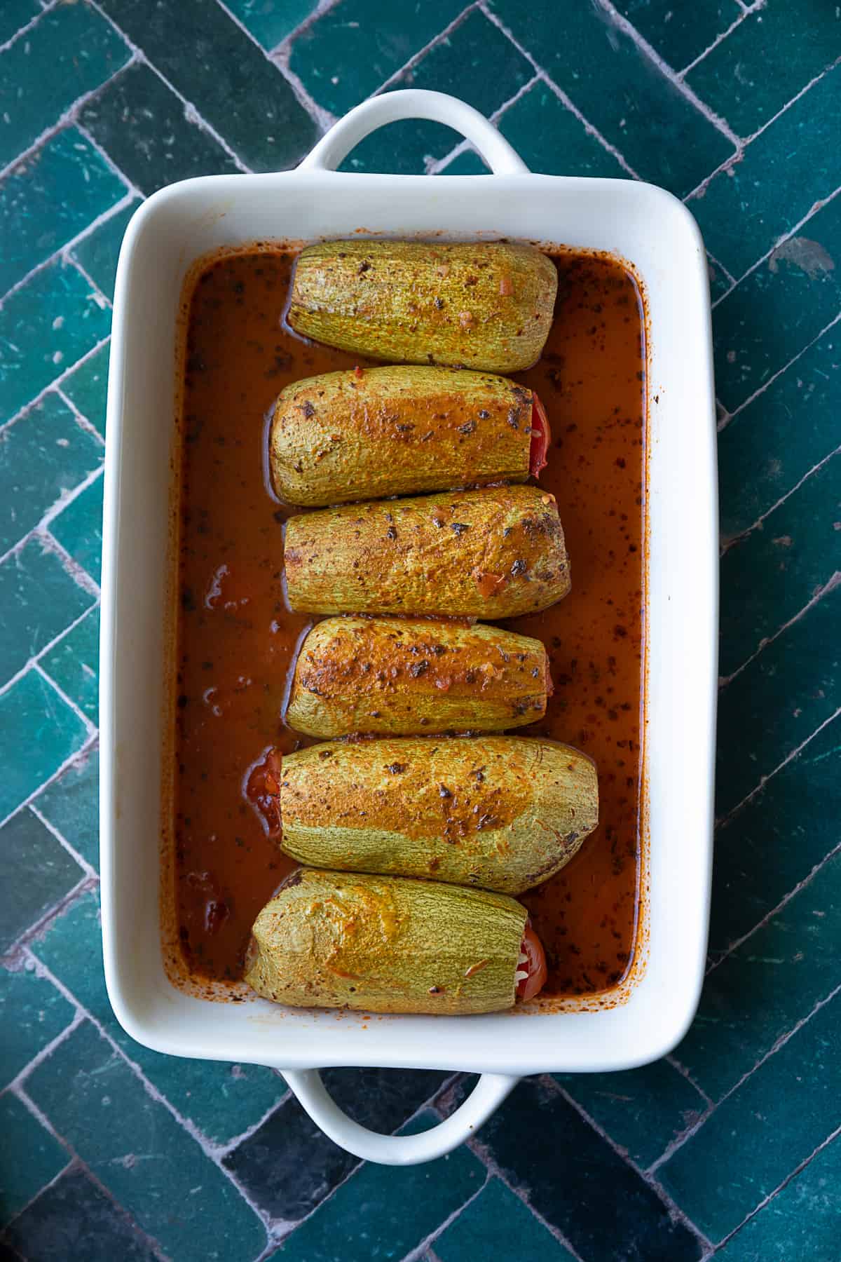 Several pieces of stuffed Mediterranean vegetables served in a shallow dish with tomato sauce.