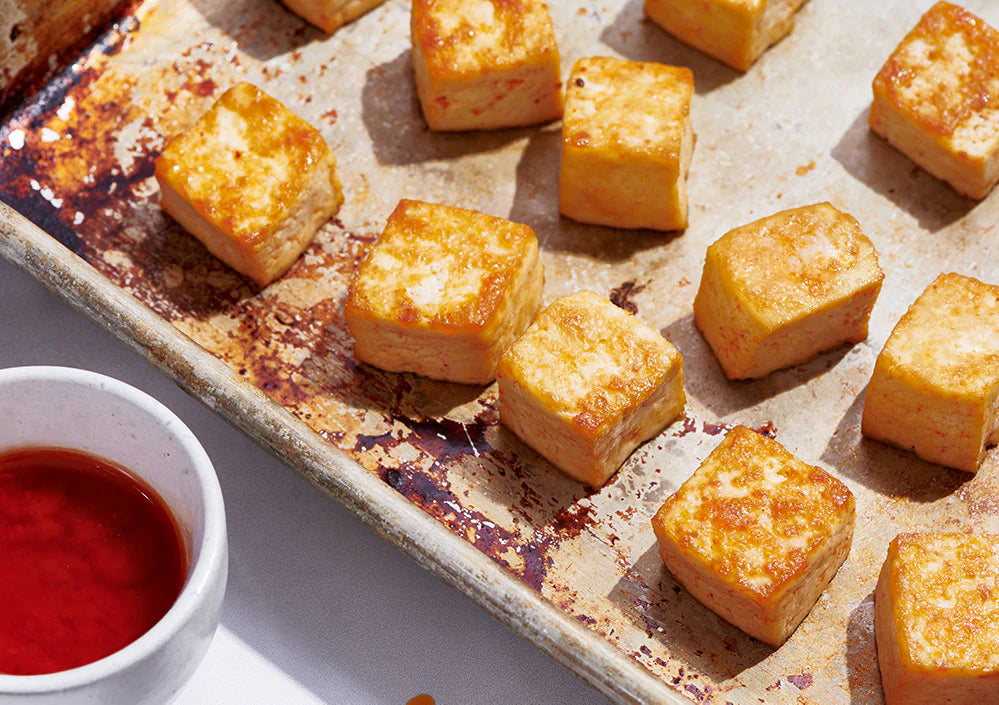 Cubed tofu spread evenly on a metal baking sheet for roasting.