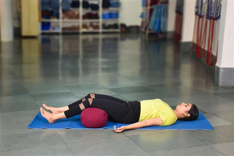 A person in a restorative Savasana pose using a yoga bolster for comfort.