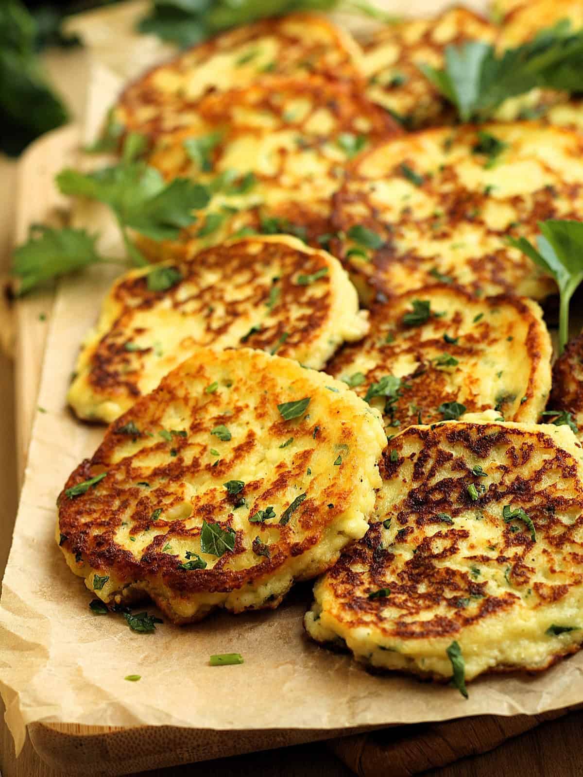 A pile of golden-brown ricotta fritters on a wooden serving board garnished with fresh parsley.