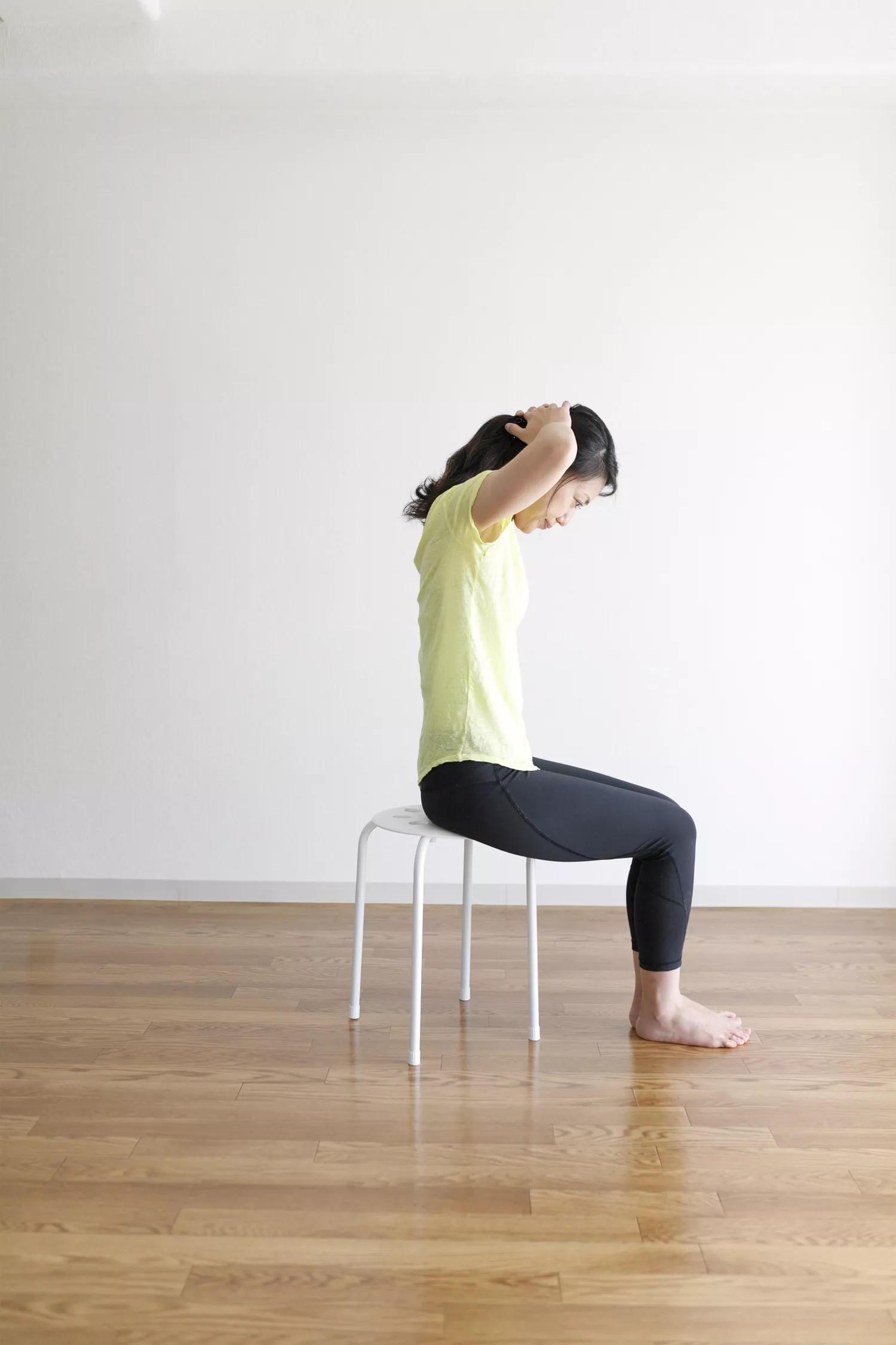 A side view of a person performing the seated cat-cow stretch on a chair.