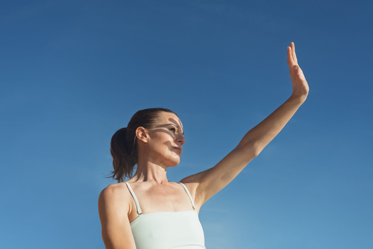 A person outdoors in the sun shielding their eyes with their hand.