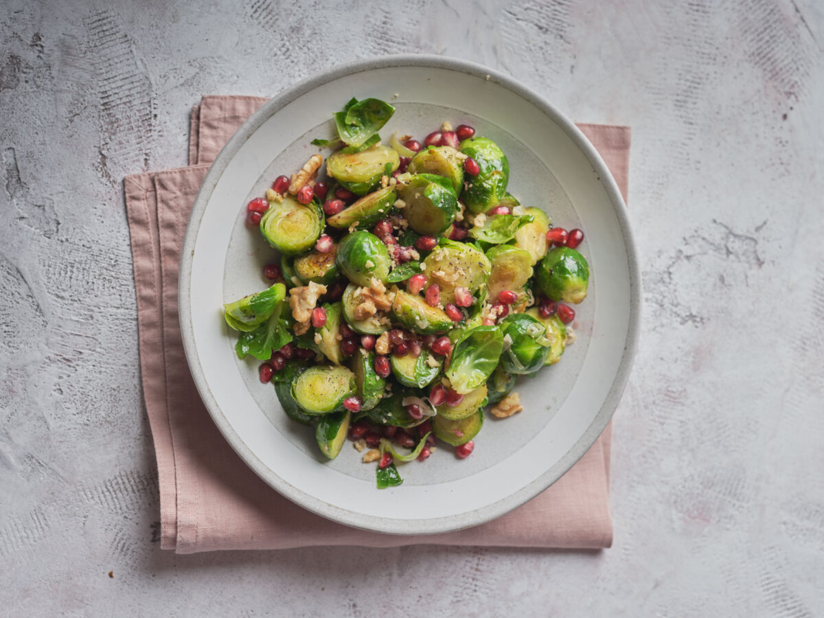 A close-up view of a bowl of Brussels sprouts mixed with pomegranate seeds and walnuts.