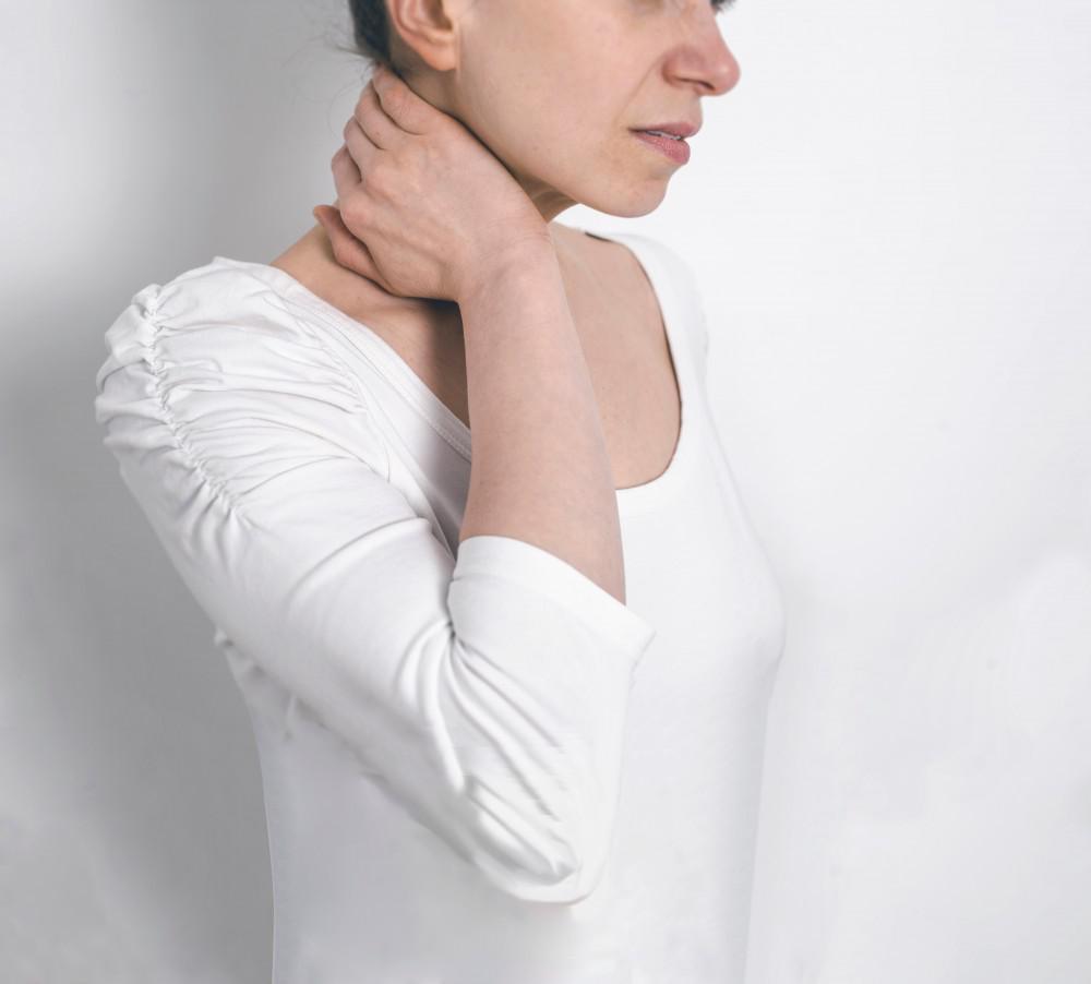 A person rubbing their neck and shoulder area to relieve muscle tension.