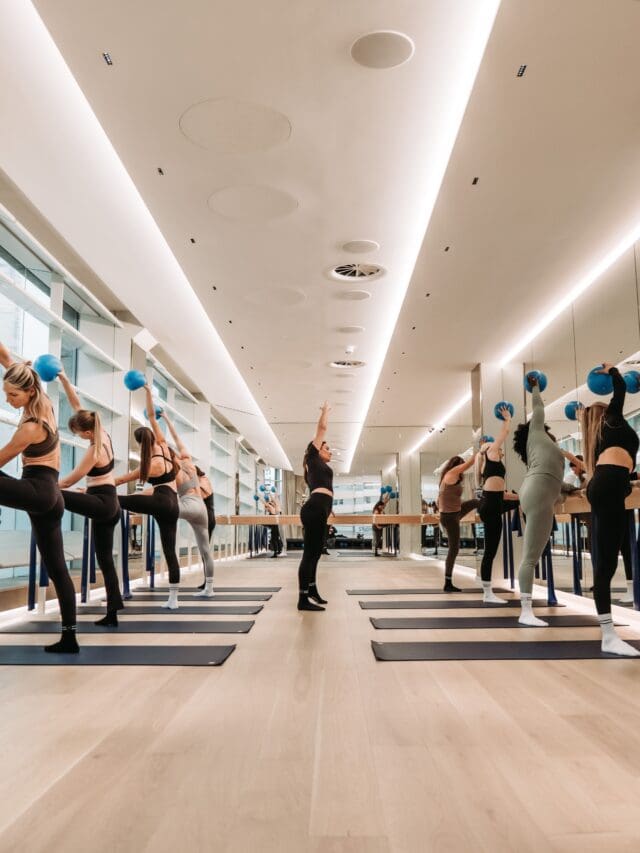 A group of women in a barre class performing synchronized exercises.