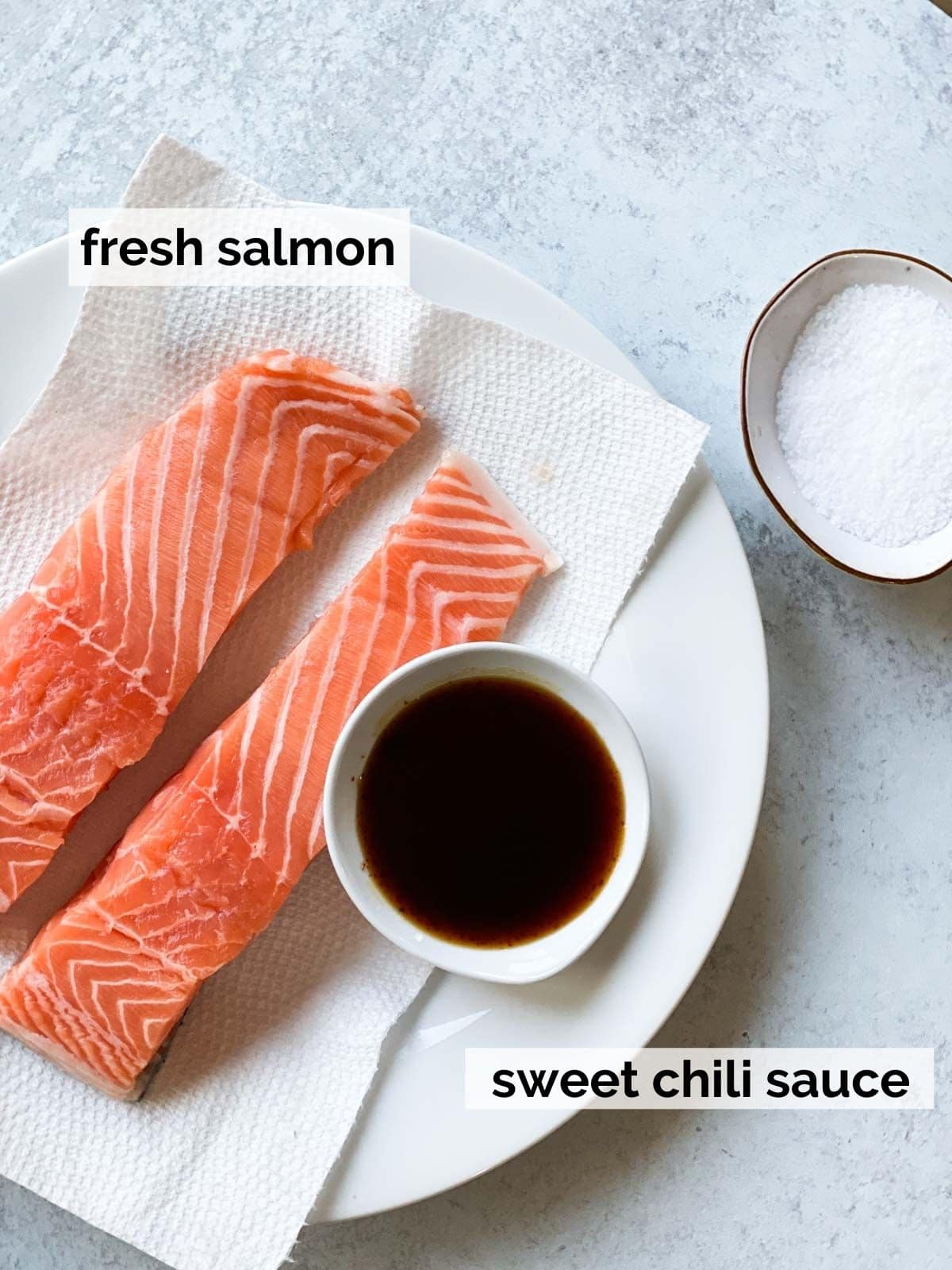 Raw salmon fillets placed next to a glass jar of sweet chili sauce on a kitchen counter.