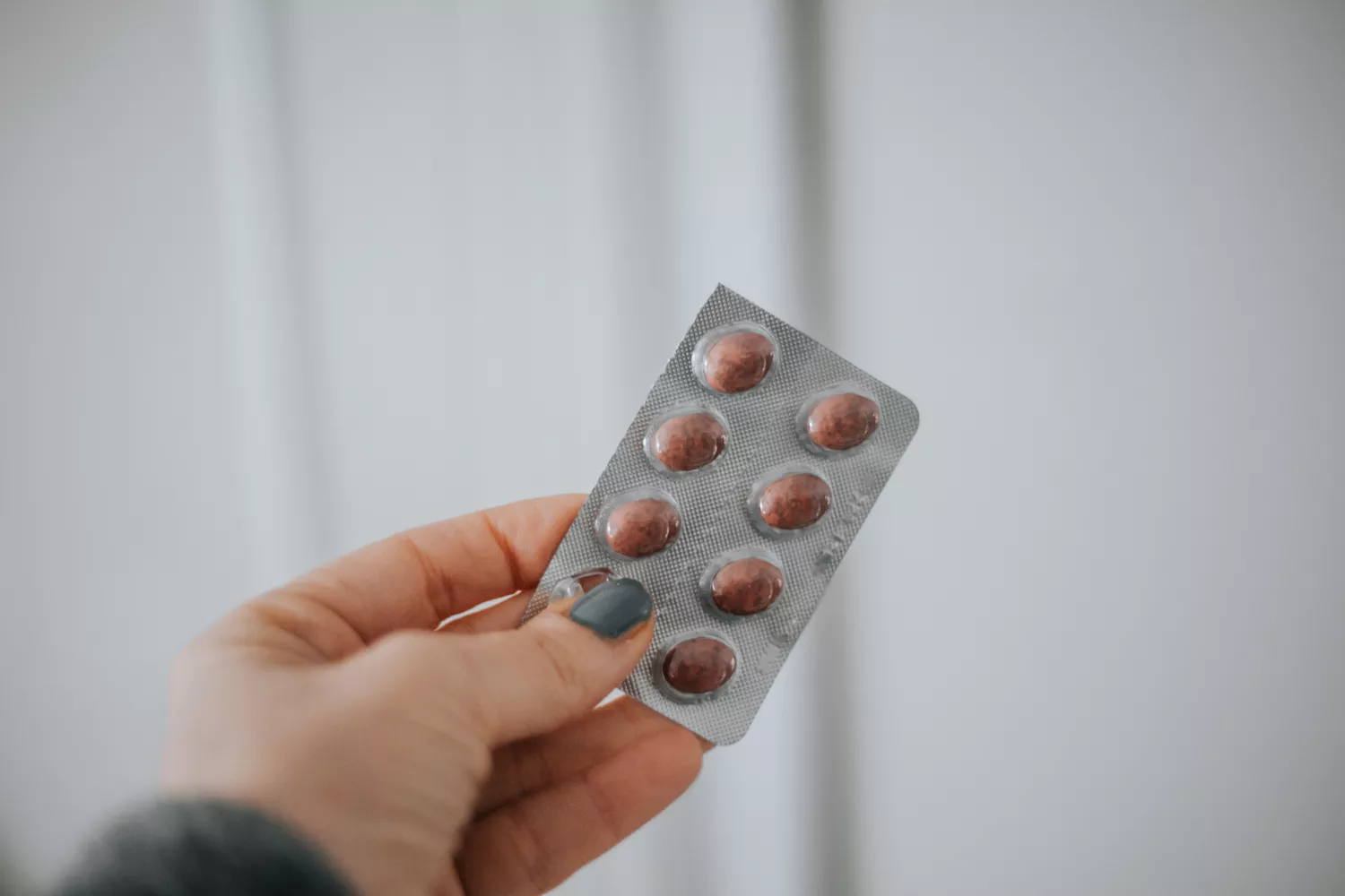 A woman holding a blister pack of nutritional supplements to support skin structural health.