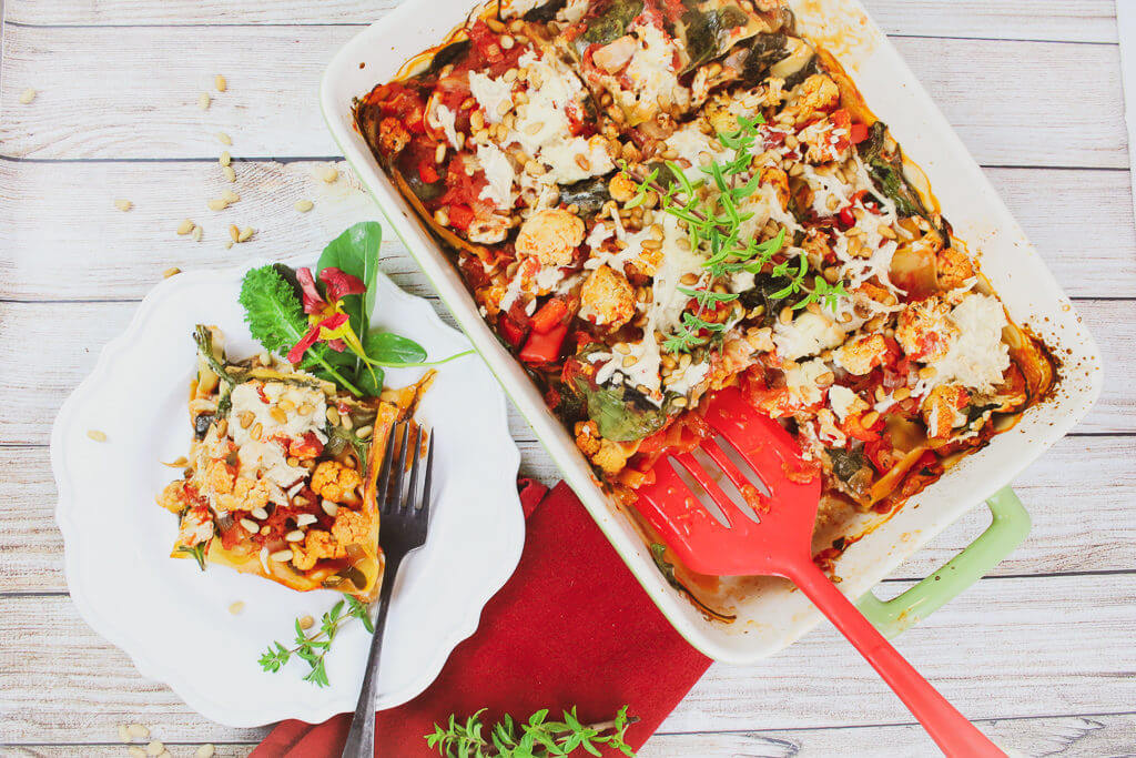 A baked cauliflower lasagna in a ceramic dish showing layers of vegetables and sauce.