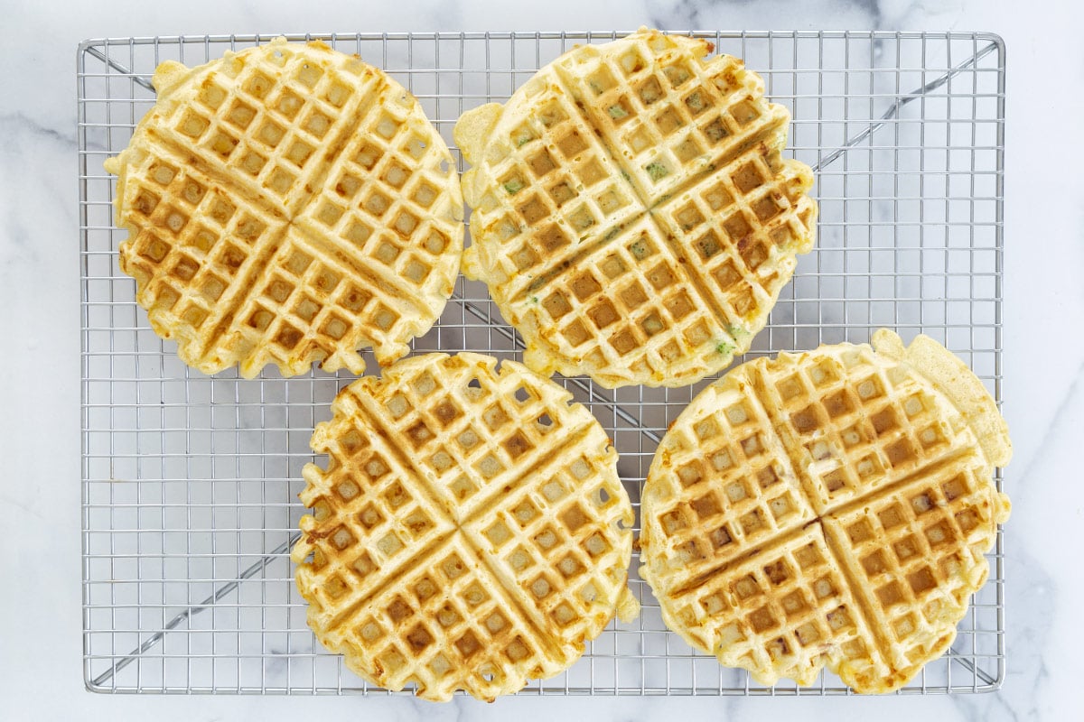 Several savory waffles resting on a metal wire cooling rack to prevent sogginess.