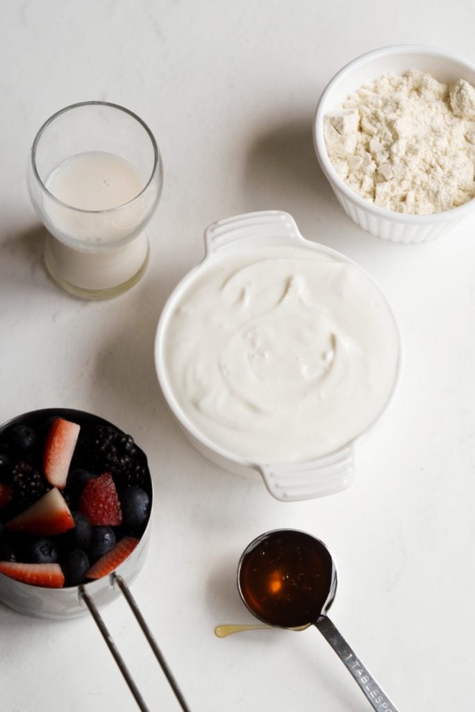 Overhead view of yogurt, milk, fresh berries, and protein powder ingredients.