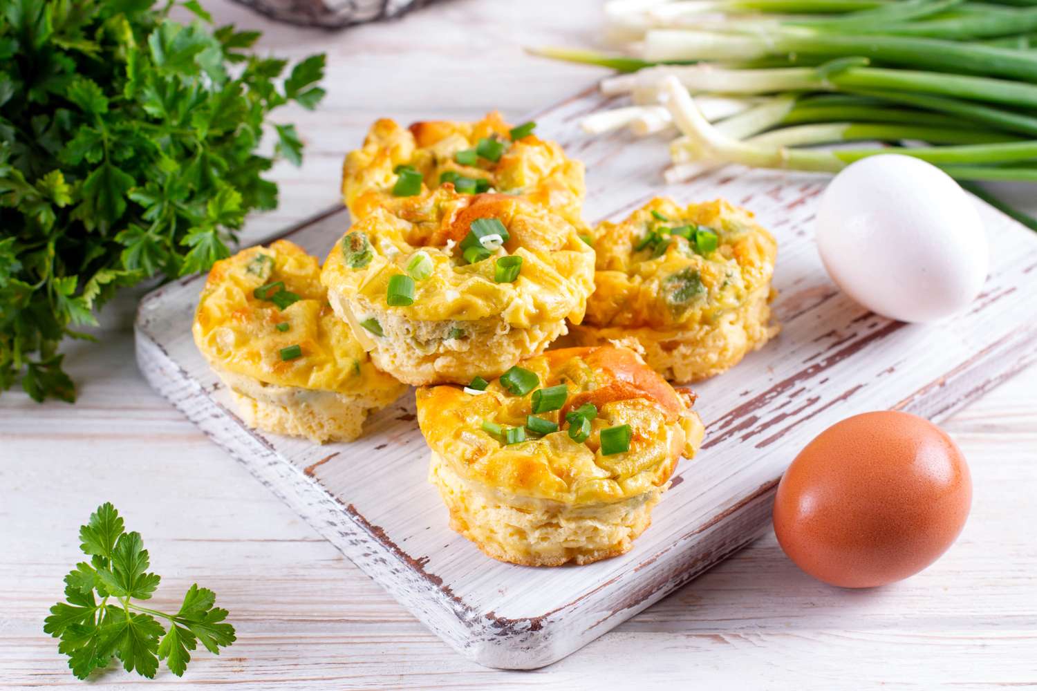 Freshly baked egg muffins with green onions on a white wooden board.