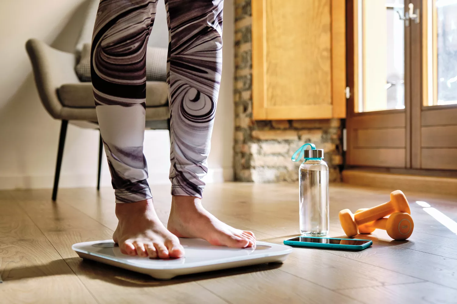 A person at home monitoring their body weight on a scale as part of a lifestyle intervention plan.