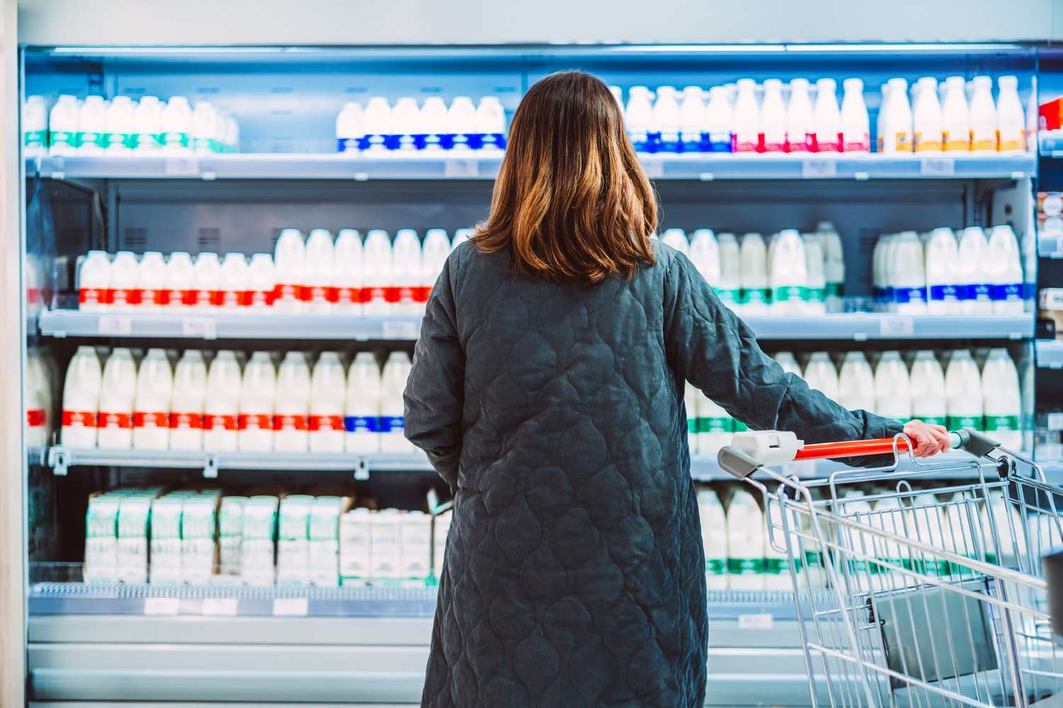 A person browsing the health and dairy section of a grocery store from behind.