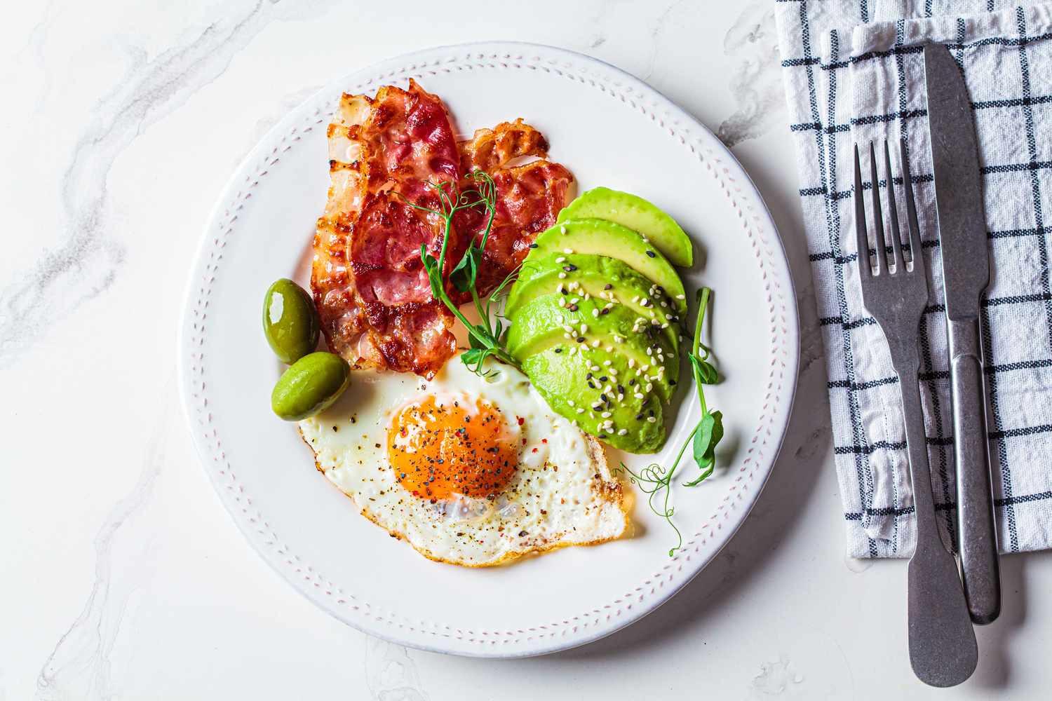 A healthy meal with a fried egg, avocado, bacon, and olives representing dietary choices monitored by CGM users.
