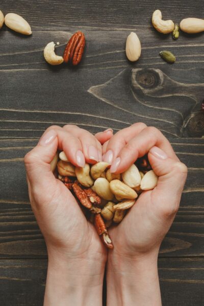 Human hands forming a heart shape while cradling a pile of pecans.