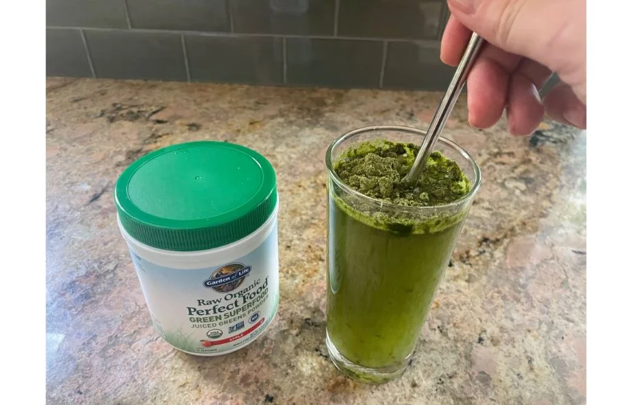 A close-up of green powder being stirred and dissolved into a glass of water.
