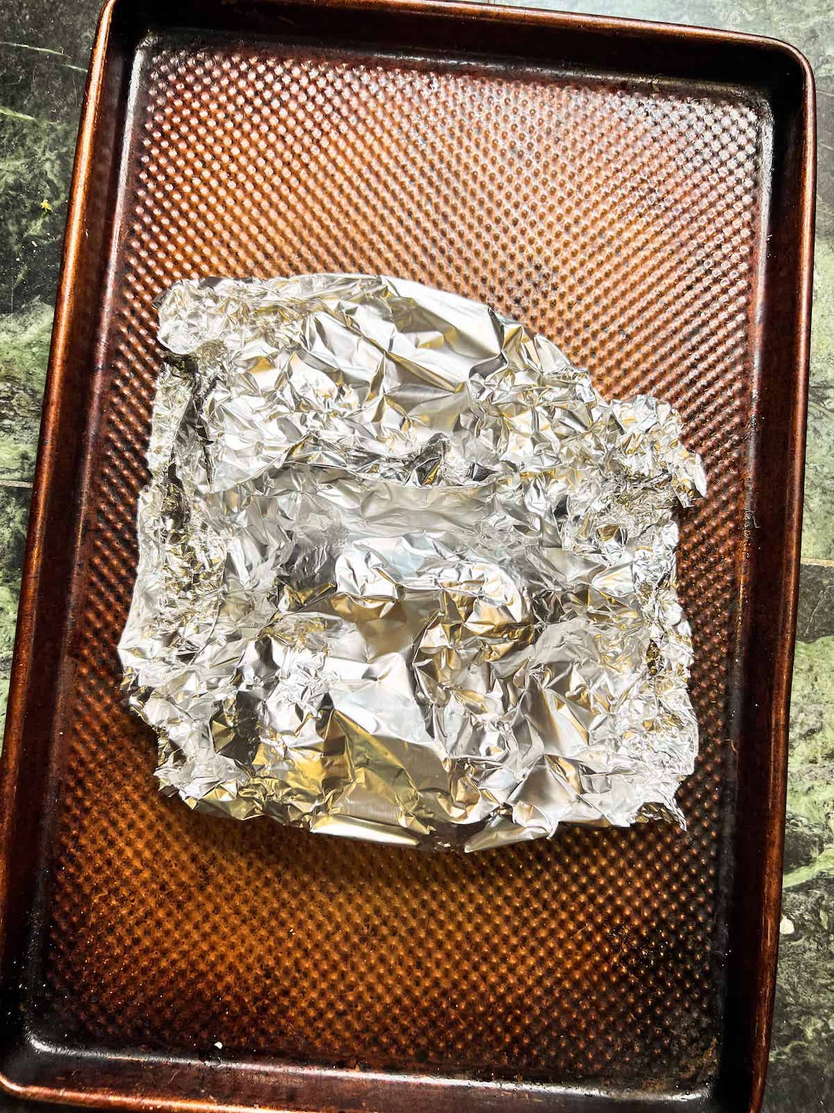 Beets wrapped and sealed in a silver aluminum foil packet on a metal baking sheet.