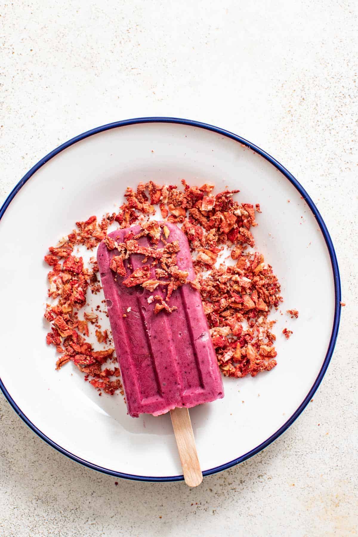 Pressing a frozen purple popsicle into a plate of crushed freeze-dried strawberries.