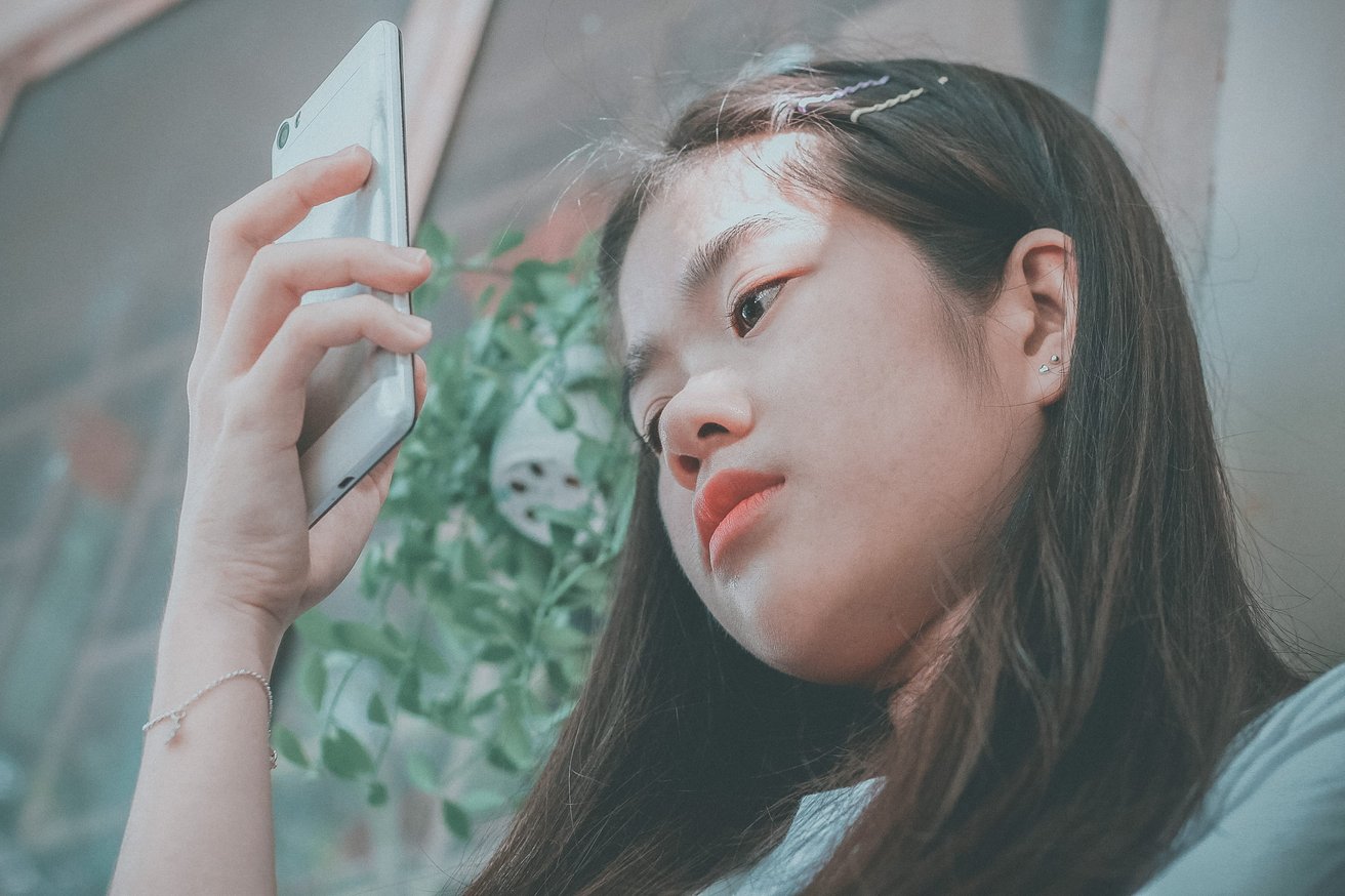 A young woman appearing concerned while looking at her smartphone.