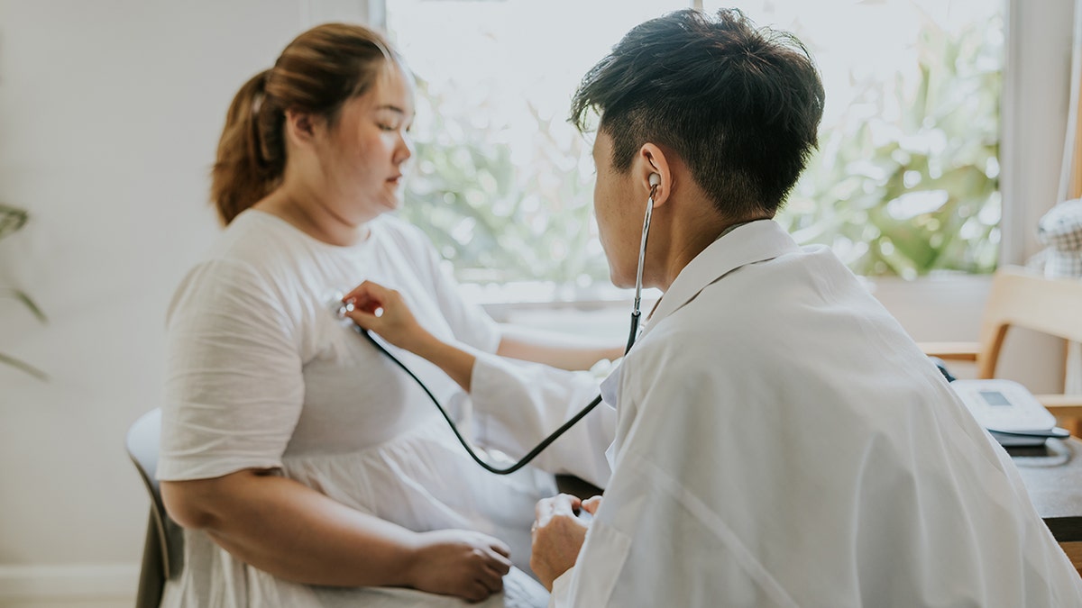 A healthcare provider using a stethoscope to check a patient's heartbeat during a consultation.