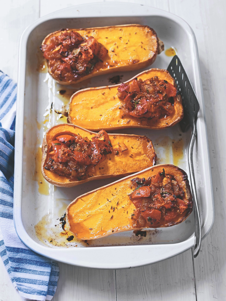 A close-up of a stuffed butternut squash with a savory filling and fresh herb garnish.