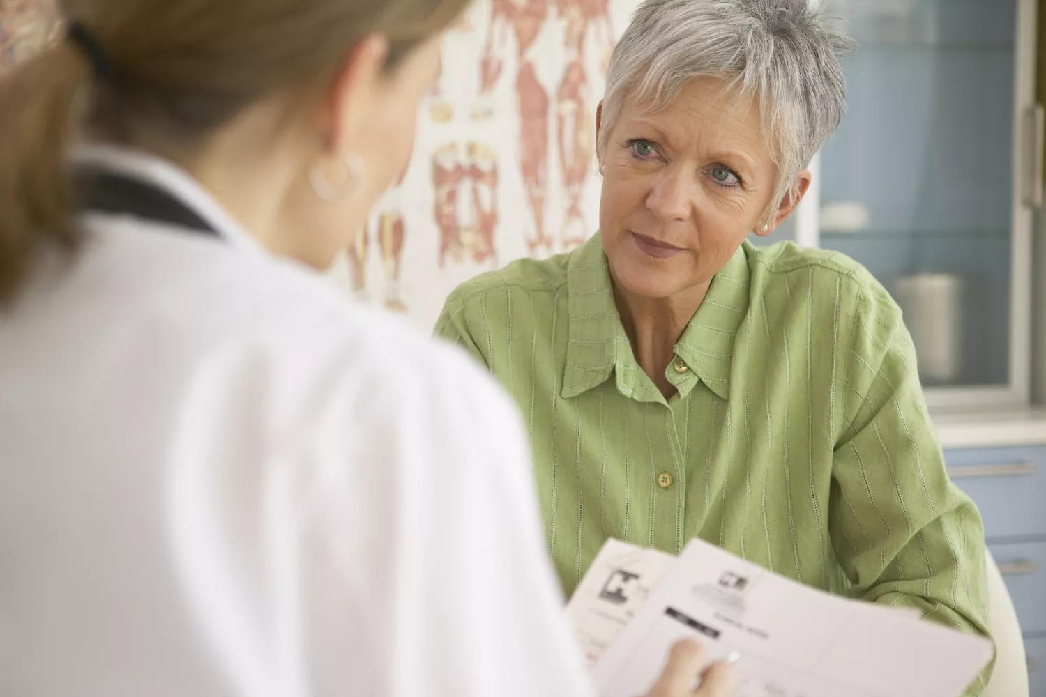 A senior woman sitting in a bright clinical office discussing treatment documents with her healthcare provider.
