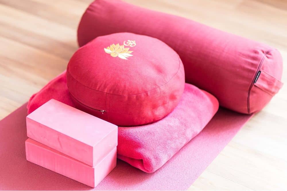 A coordinated set of pink yoga props including a mat, blocks, and a bolster.