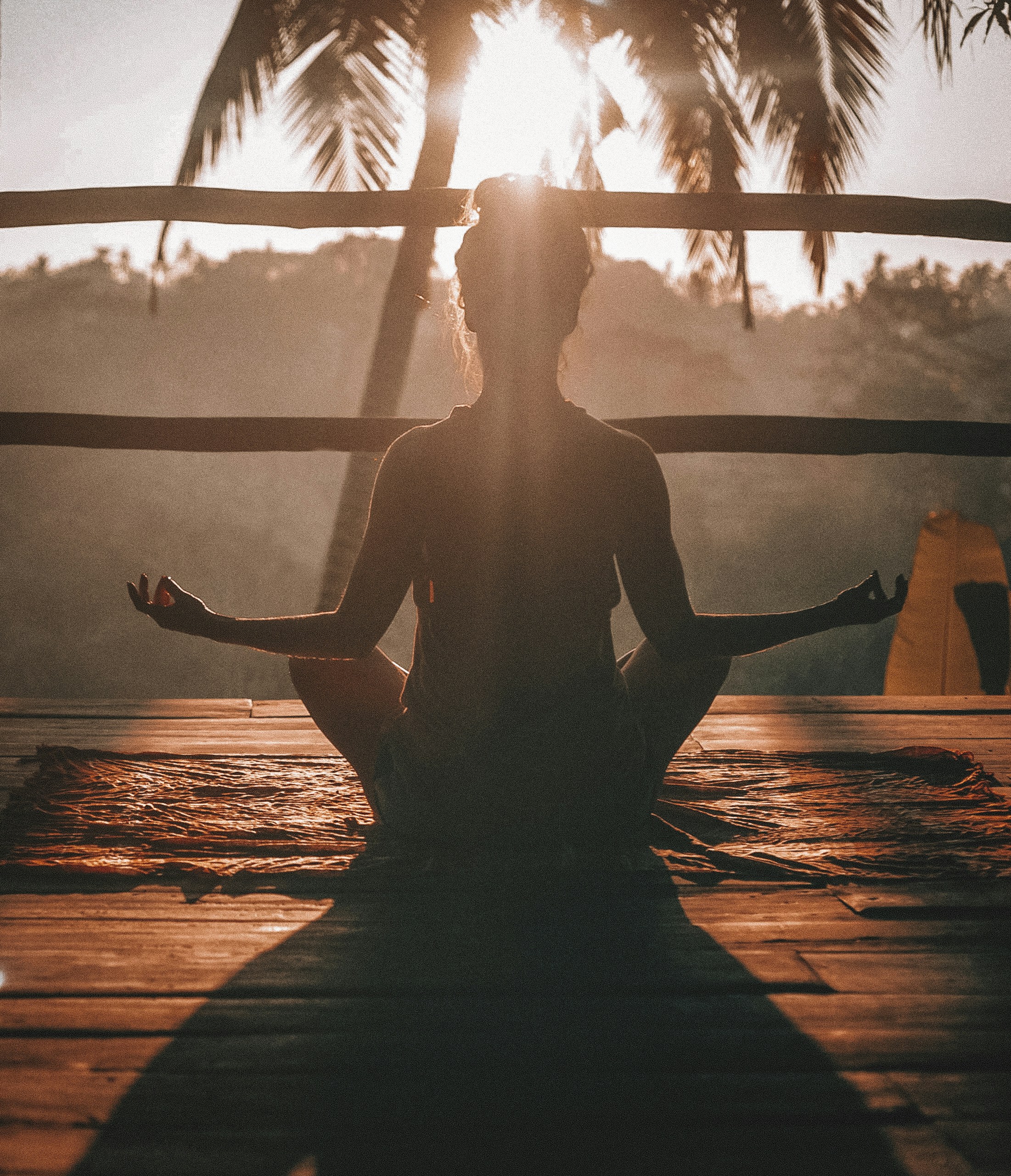 A woman sitting cross-legged in a meditative pose with her hands placed over her heart and torso.