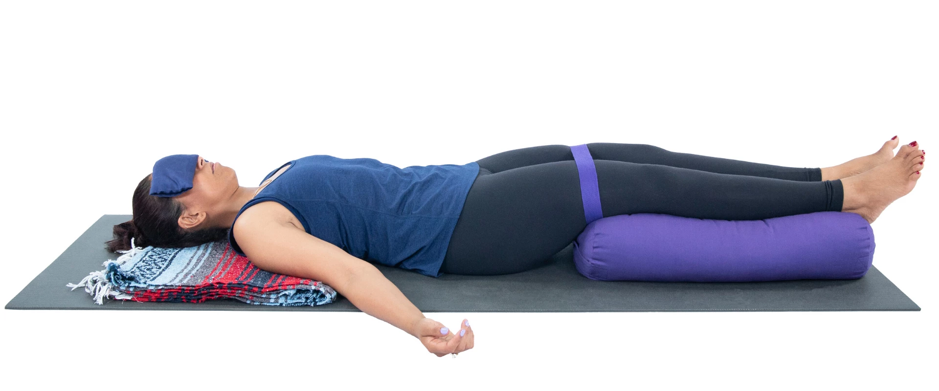 A woman lying in Savasana pose supported by a yoga bolster under her knees.