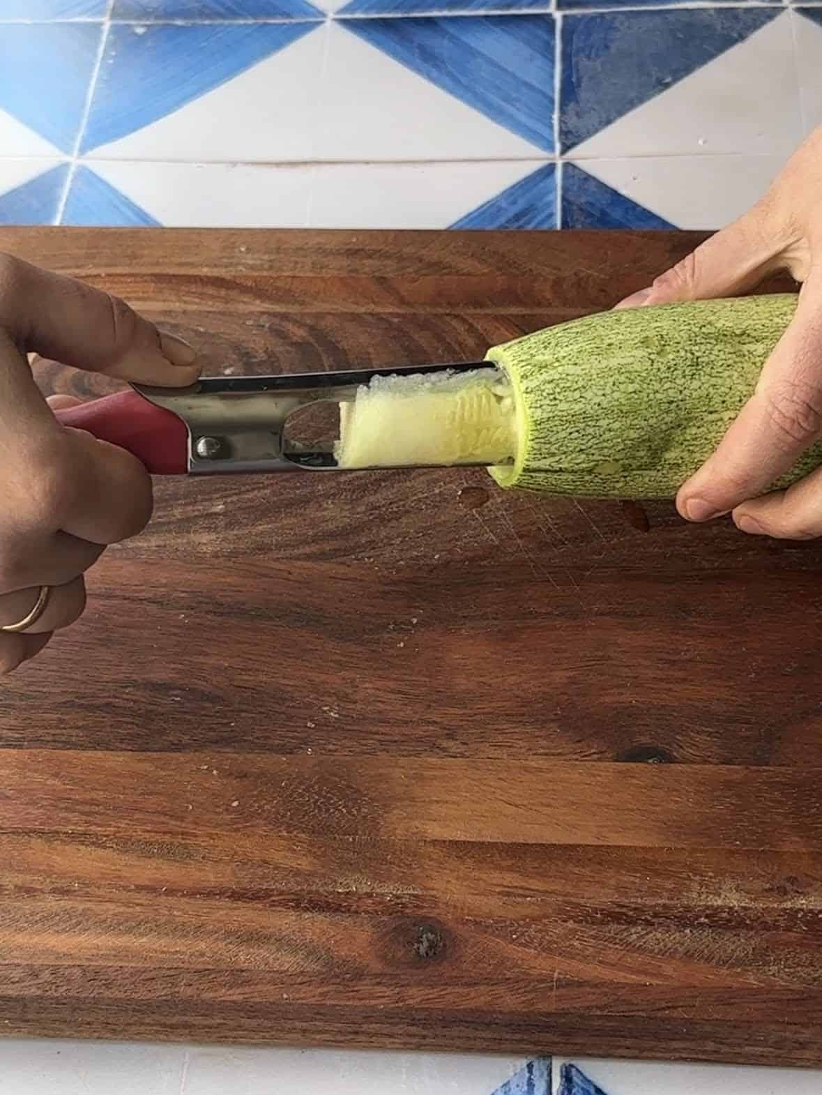 A hand using a tool to hollow out the center of a vegetable for a stuffing recipe.